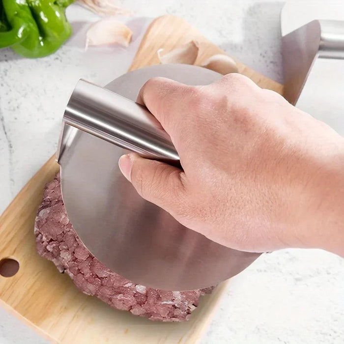 A stainless steel grill press being used to flatten minced meat on a wooden cutting board, emphasizing its sturdy and efficient design.