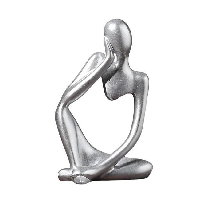 Silver minimalist abstract sculpture of a figure sitting cross-legged with one arm resting on the head.