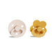 A round, beige pacifier with a ring handle next to a yellow, flower-shaped pacifier with a ring handle.