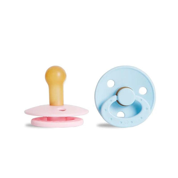 A pink pacifier with a beige nipple and a blue, round pacifier with a ring handle.