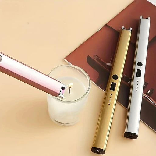 A pink plasma lighter being used to light a candle, with two additional plasma lighters (gold and silver) lying nearby on a beige surface with a magazine.