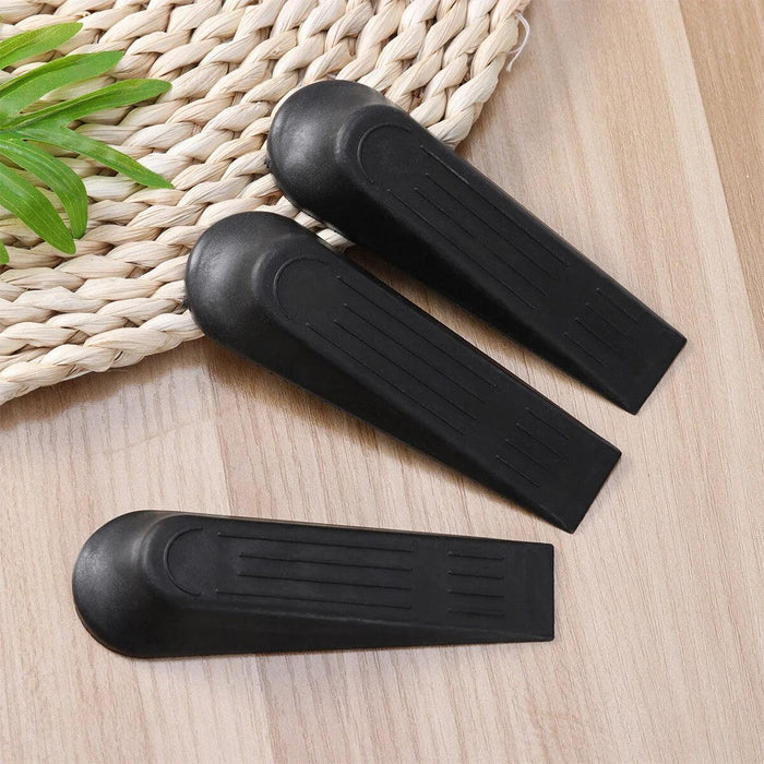 Three black rubber door stoppers placed side by side on a light wooden surface, with a woven mat and green plant in the background, emphasizing their sturdy, functional design.