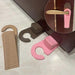 A set of three wedge-shaped door stoppers in brown, pink, and beige, featuring a hook design for hanging on door handles, shown in use under a door to prevent it from closing. A close-up inset highlights the stopper hung on a door handle.