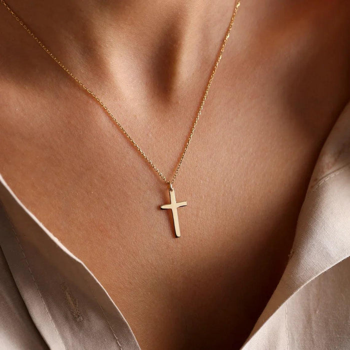 Close-up of a gold cross necklace hanging around a person's neck, set against a backdrop of their skin and a light-colored top.