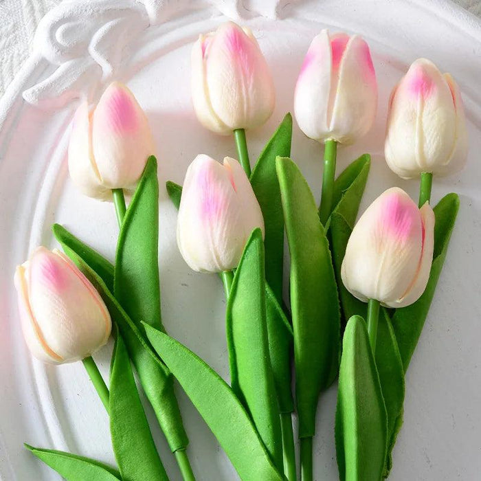 A bouquet of light pink tulips with green leaves on a white plate.