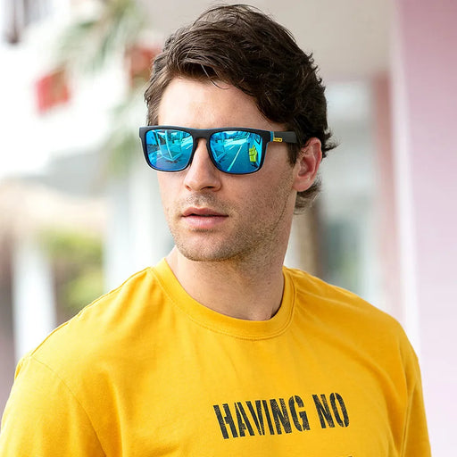 Rectangular sunglasses with black frames and blue mirrored lenses, worn by a man in a yellow shirt.