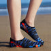 A person wearing blue water shoes with black and red accents, standing on the beach near the water.