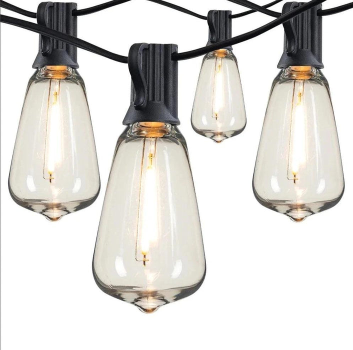 A close-up view of a string of vintage-style Edison light bulbs hanging on black cables. The bulbs are illuminated, emitting a warm, yellowish light, and their clear glass reveals the glowing LED filaments inside. The black bulb holders and cables add a contrasting, modern touch to the classic bulb design.