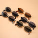  Multiple pairs of oval sunglasses with gold frames and dark lenses arranged on a peach-colored surface.