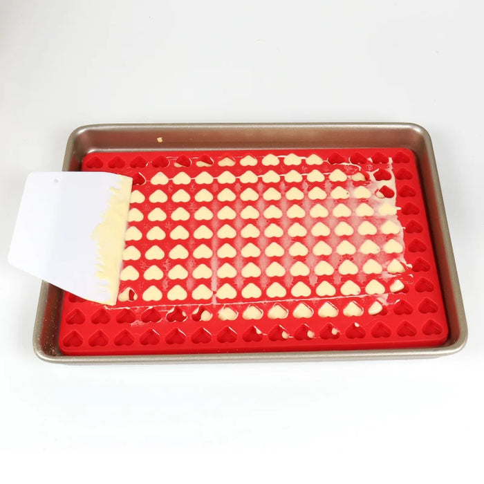 Red heart-shaped silicone mold on a baking tray filled with dough.