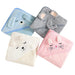 Four folded baby towels, each with a hood featuring an embroidered animal face. The towels are in light blue (dog), grey (elephant), cream (bear), and pink (cat). Each towel has embroidered details to represent the animal's face and ears.