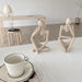 Two abstract sculptures in contemplation poses are placed on a white table next to a coffee cup and saucer.