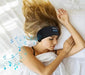 A woman with long blonde hair is sleeping on her side in bed, wearing a black headband with built-in Bluetooth headphones, indicated by musical notes emanating from the headband.