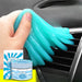 A hand using blue cleaning gel to clean the air vent of a car, with a pack and a container of the gel shown in the foreground.