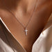 Close-up of a silver cross necklace hanging around a person's neck, set against a backdrop of their skin and a light-colored top.