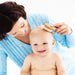 A woman brushing a smiling baby's hair with a wooden baby hairbrush.