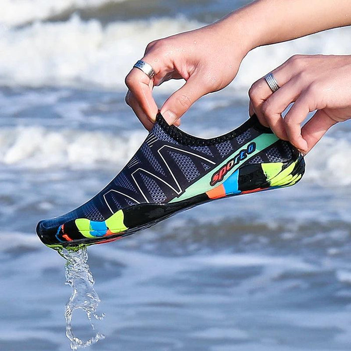 Hands holding a black and blue water shoe, allowing water to drain from the shoe, with the ocean in the background.