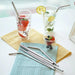 Stainless steel metal straws in glasses with drinks and fruits, placed on napkins on a white table.