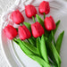 A set of seven artificial red tulips with green leaves, displayed on a white decorative plate.