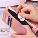 A close-up of hands holding a pink wallet, inserting coins into its zippered compartment. The wallet has multiple card slots visible.