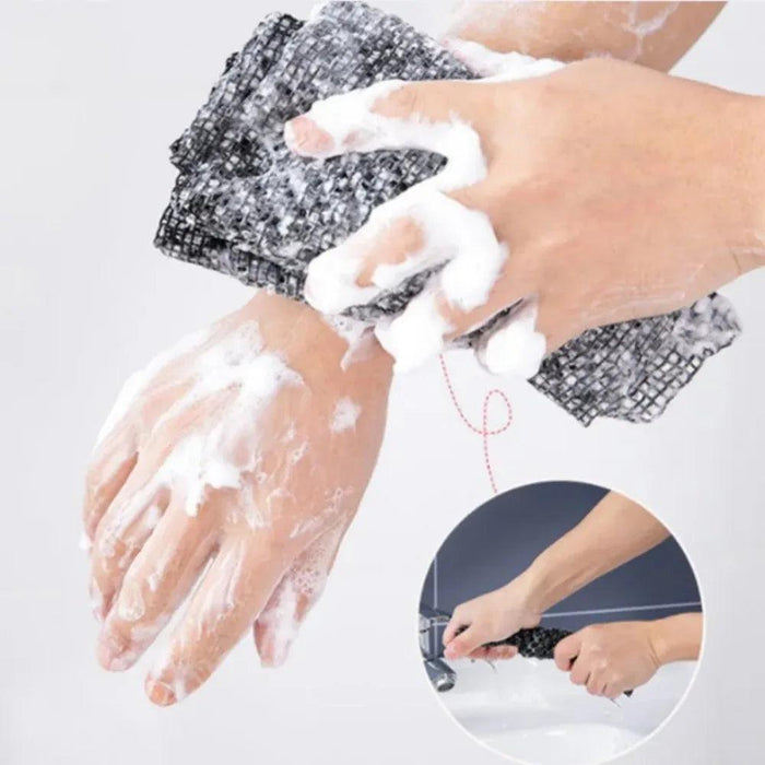 A person washing their arms with a black exfoliating towel, creating a lather of soap.