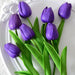 A bouquet of deep purple tulips with green leaves on a white plate.