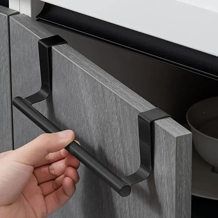 a close-up of a black over-the-door towel rack installed on a gray cabinet door. The rack has a simple, modern design and fits snugly over the cabinet, providing a convenient spot to hang towels in the kitchen or bathroom.