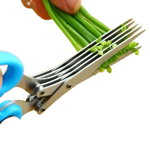 Green-handled herb scissors being used to cut chives on a wooden cutting board.