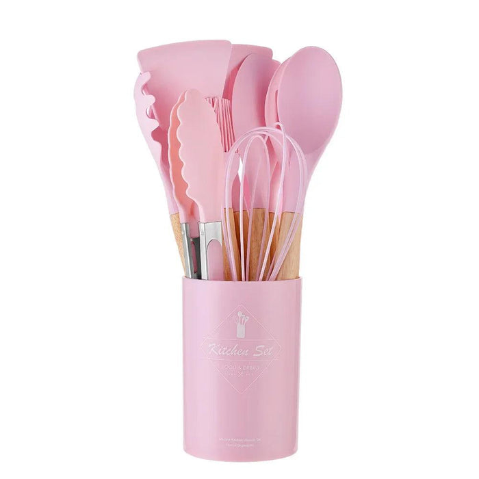 A set of pink silicone kitchen utensils in a matching holder.