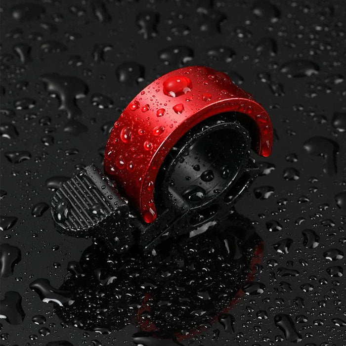 Red Bicycle Bell shown with water drops on it, displayed on black wet surface.