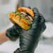 A close-up image showing a person wearing black gloves while holding a freshly made sandwich. This emphasizes the importance of hygiene and safety in food handling.