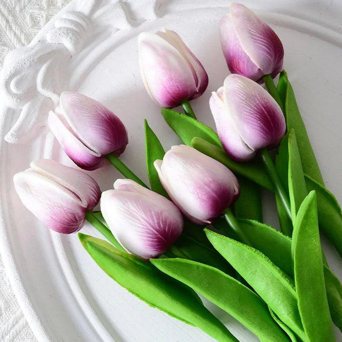 A bunch of tulips with a gradient of purple to white petals, arranged on a white plate.