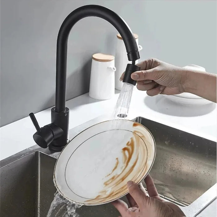 A person holding a white plate under a faucet fitted with a black attachment, rinsing off residue in a kitchen sink.