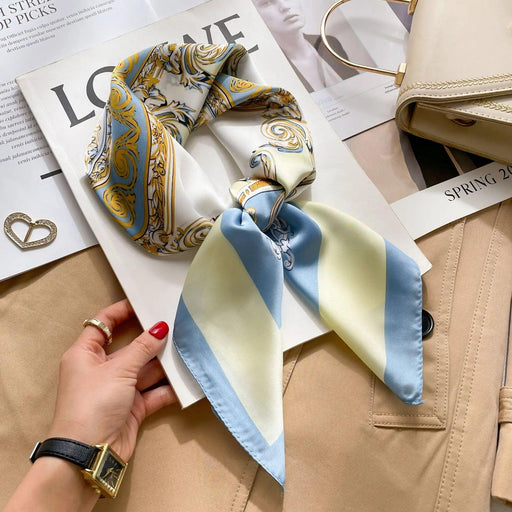 Close-up of a white and gold patterned silk scarf with blue and green accents, neatly tied and placed on top of a book and beige coat.