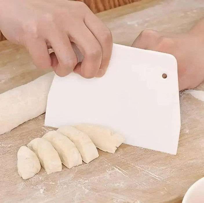 Close-up of a hand using a white dough scraper to cut dough into even pieces on a floured surface.