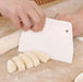 Close-up of a hand using a white dough scraper to cut dough into even pieces on a floured surface.