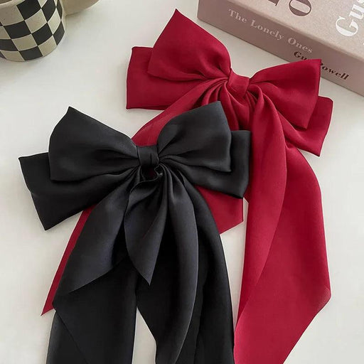 Two satin hair bows, one black and one red, laid side by side on a white surface, highlighting their elegant design with long flowing tails.