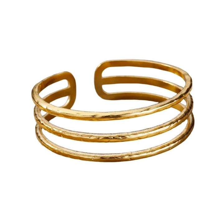 Gold cuff bracelet with three parallel bands and a hammered finish, displayed on a white background.