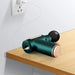 The Fascia Massager is plugged into a wall outlet with a white charging cable. The teal Fascia Massager rests on a wooden surface while charging.