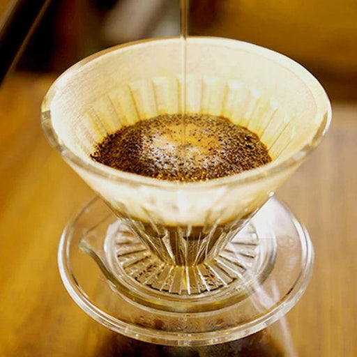 A close-up of a Crystal coffee dripper in use, with hot water being poured over coffee grounds, highlighting the brewing process.