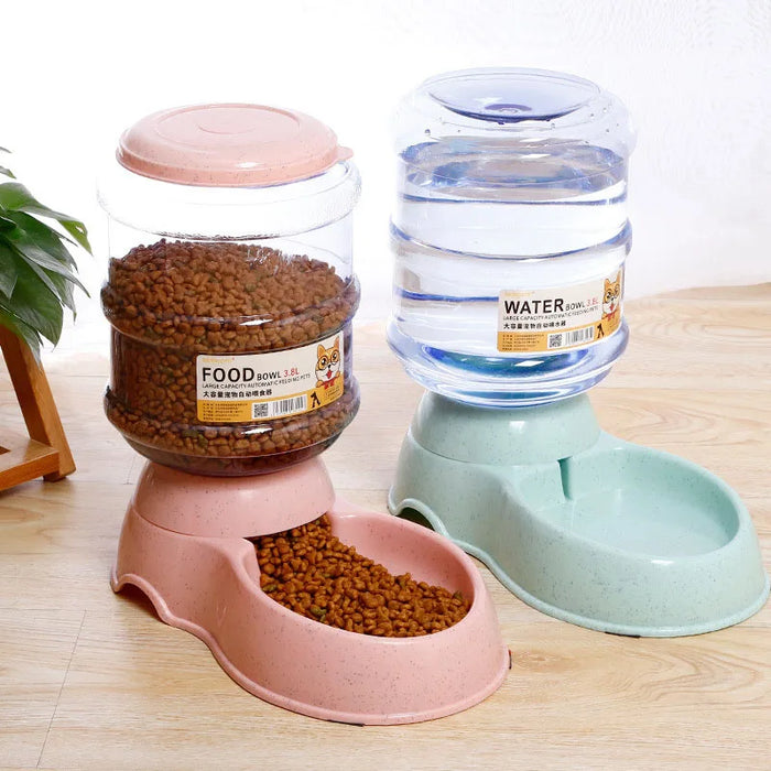 Two automatic pet dispensers, one with a pink base filled with kibble labeled "FOOD" and one with a green base filled with water labeled "WATER," placed on a wooden floor.