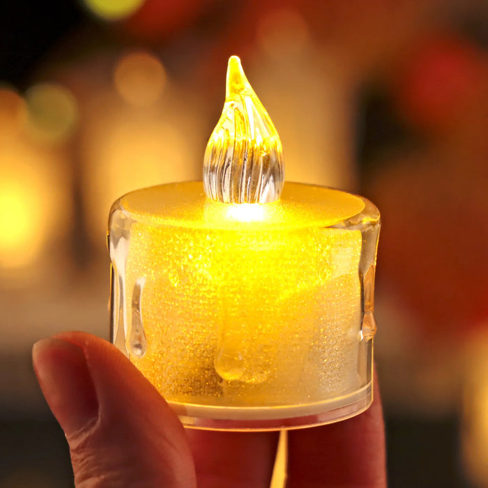 A detailed close-up of a realistic-looking LED tea light candle with a flickering flame effect. The candle emits a warm yellow glow, enhancing its resemblance to a real candle.