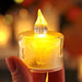 A detailed close-up of a realistic-looking LED tea light candle with a flickering flame effect. The candle emits a warm yellow glow, enhancing its resemblance to a real candle.