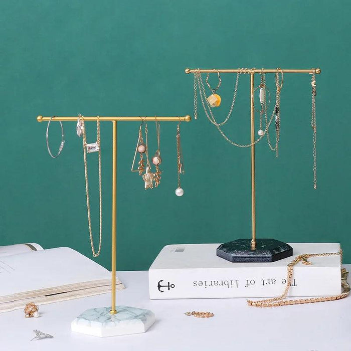 Two elegant gold jewelry stands with marble bases display necklaces and earrings against a green backdrop.