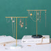 Two elegant gold jewelry stands with marble bases display necklaces and earrings against a green backdrop.