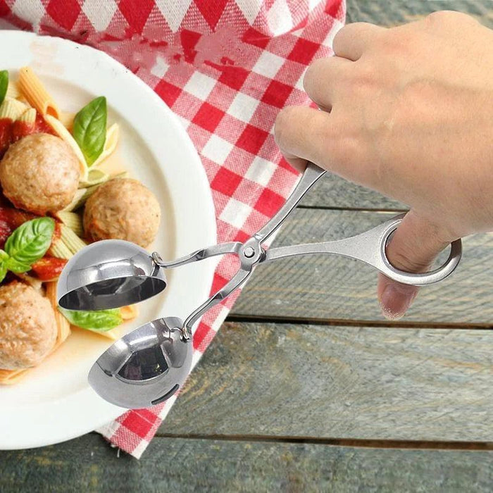 Stainless steel meatball tongs held by a person, with a plate of pasta and meatballs on a red-checkered tablecloth in the background.