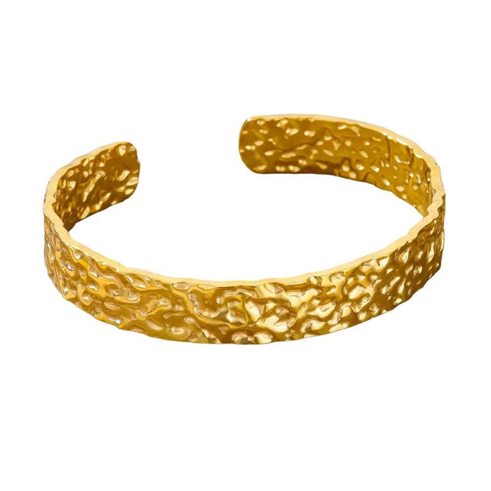  Gold cuff bracelet with a hammered texture, displayed on a white background.