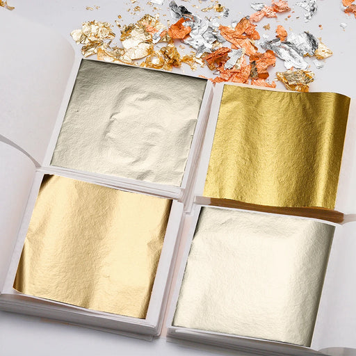 Gold, silver, and copper leaf sheets for crafting, presented in a book format with loose flakes on the side.
