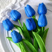 A bunch of bright blue tulips with green leaves, placed on a white plate.