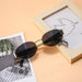 Gold-framed oval sunglasses with black lenses placed on a table next to a picture frame and a magazine.